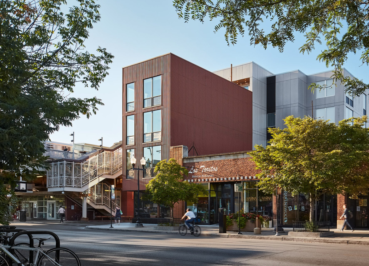 A photo of a building on a tree-lined street in Chicago. The building has many different facades: brick, metal, and more modern siding.